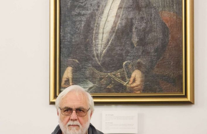 Starszy mężczyzna pozuje do zdjęcia na tle portretu w Zamku.