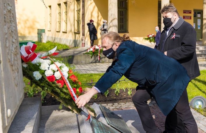 Dyrektor jan Godłowski składający wieniec z biało-czerwonych kwiatów pod pomnikiem.