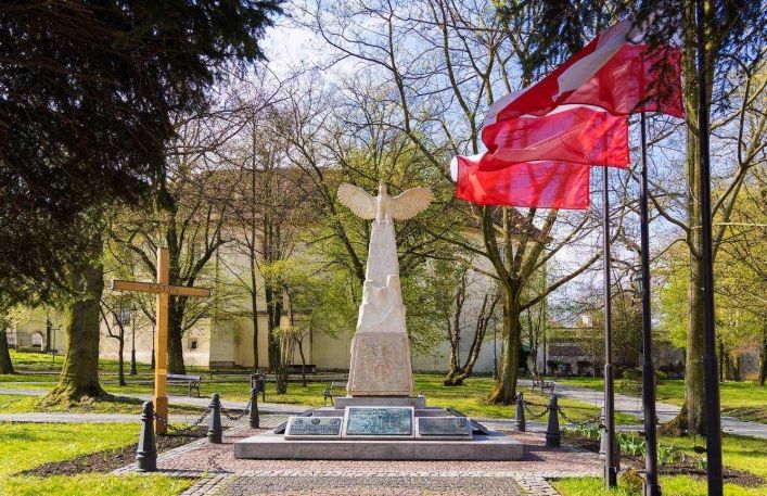 Pomnik Odrodzenia Polski w Wieliczce. obok powiewają biało-czerwone flagi.