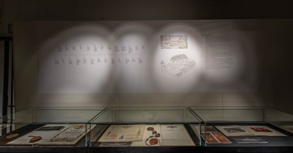 Oświetlona ściana z rysunkiem Zamku Żupnego oraz osią czasu. poniżej gabloty z dokumentami, fotografiami i pieczęciami.