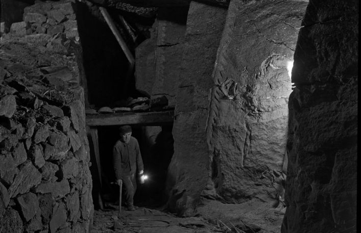 Pochylona postać wychodzi z chodnika w kopalni.