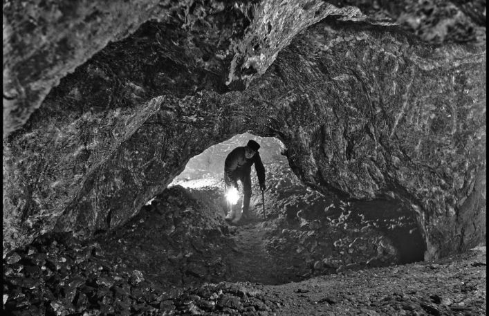 Schylony mężczyzna z zapaloną lampą górniczą przechodzi przez niskie przejście w solnej ścianie.