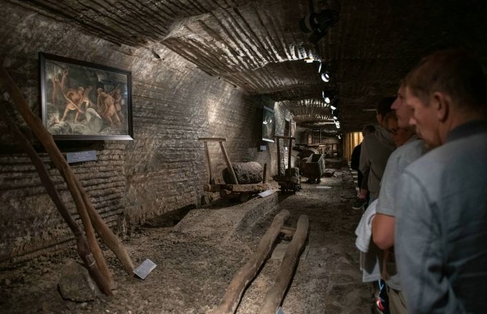 Turyści oglądają obrazy oraz narzędzie i urządzenia do transportu poziomego w kopalni.