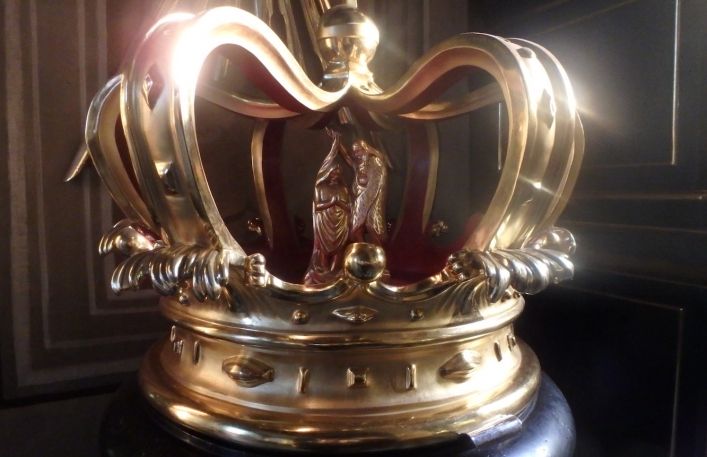 Złota korona na podstawce.W środku dwie figury świętych.
