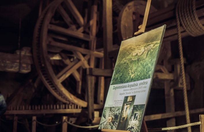 Na sztaludze plakat reklamujący wystawę: Zapomniana kopalnia srebra - historia odkrycia w 2005 roku kopalni Amalia w Srebrnej Górze; Iwona i Jan Duerschlag; 8 kwietnia- 7 czerwiec 2022 roku. W tle kierat.