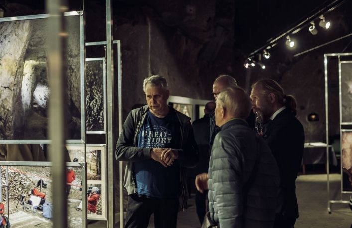 Grupa mężczyzna wraz z Dyrektorem Muzeum ogląda prezentowane fotografie