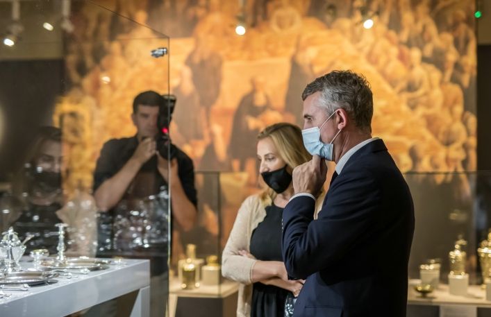Burmistrz Miasta Wieliczki wraz z młodą kobietą oglądają wystawę. W tle fotograf robi im zdjęcie.