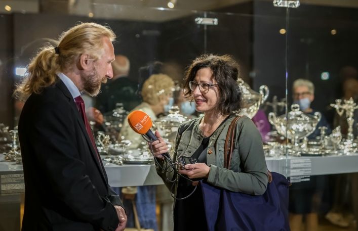 Dyrektor Muzeum udziela wywiadu dziennikarce z mikrofonem w dłoni w sali wystaw.