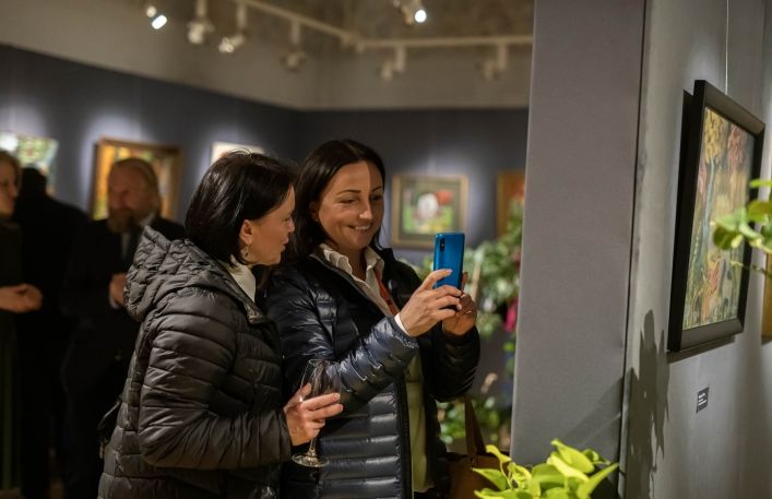 Dwie uśmiechnięte kobiety fotografują telefonem obraz podczas wernisażu
