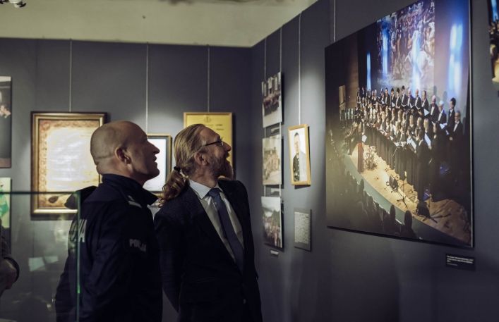 Dyrektor Muzeum wraz z komendantem oglądają fotografie z występu chóru Lutnia na wystawie czasowej w Zamku.