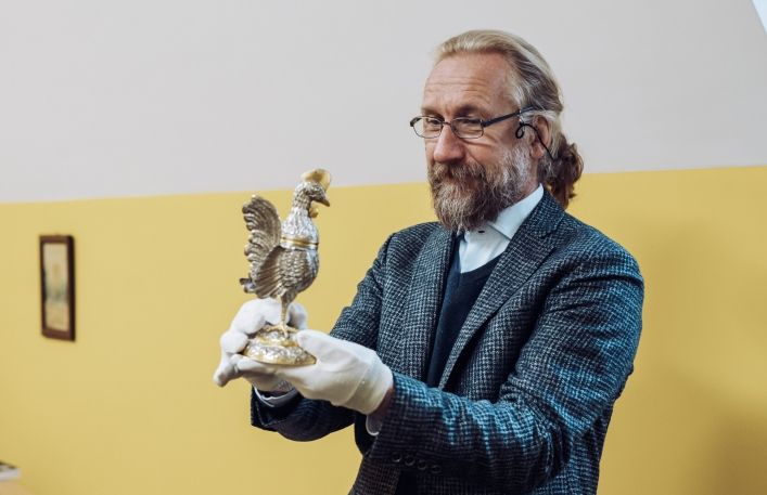 Dyrektor Muzeum Jan Godłowski trzyma w rękach w rękawiczkach nową solniczkę w kształcie koguta.