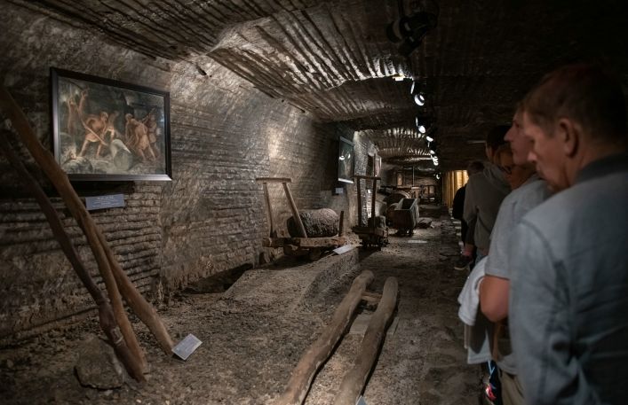 Turyści oglądają wystawę w podziemnej ekspozycji: drągi walackie, wózki zwane psami węgierskimi oraz skrzynie do transportu soli.