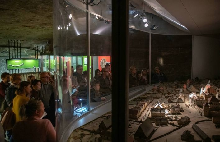 Duża grupa turystów ogląda makietę miasta Wieliczka na wystawie w podziemnej ekspozycji muzeum.