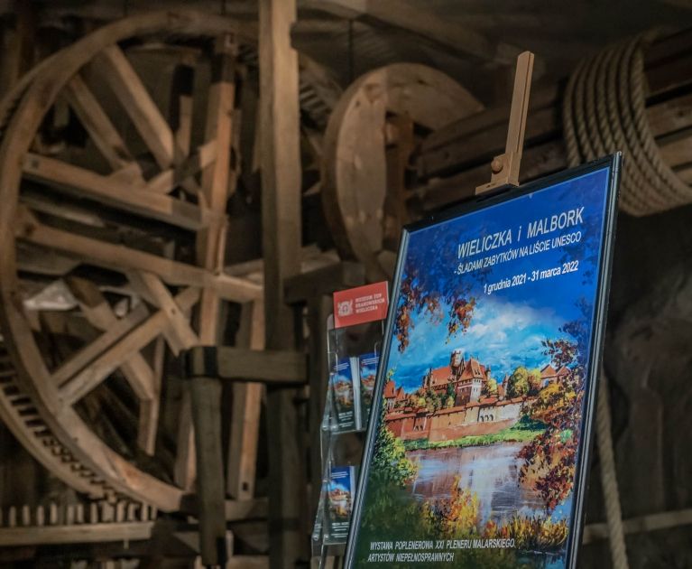 wernisaż wystawy w Kopalni Soli, plakat wystawy w tle drewniana maszyna górnicza