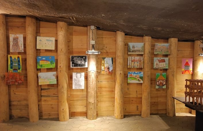 Powieszone prace konkurskowe na drewnianych obudowach w ekspozycji podziemnej Muzeum.