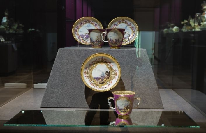 Gablota na wystawie- trzy filiżanki do czekolady wraz ze spodkami. Całość dekorowana w fioletowy kolorze ze złotymi elementami.