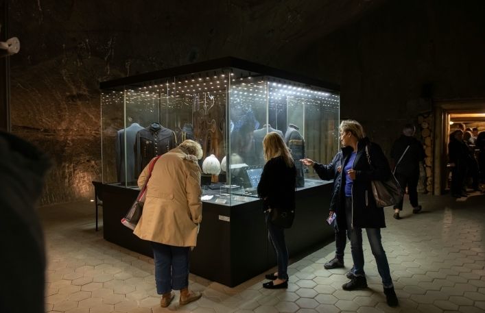 Turyści oglądają mundury górnicze w gablotach na wystawie.
