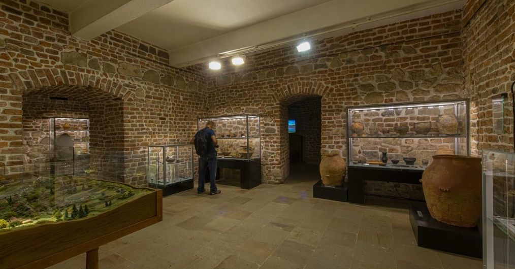 Widok dawnej sali archeologicznej. W tle zwiedzający, gabloty oraz fragment makiety.