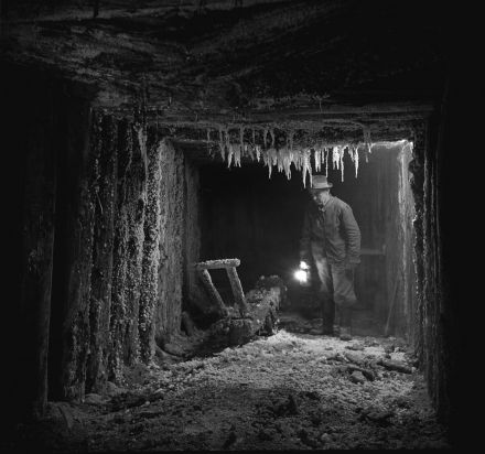 Seria czarno- białych zdjęć przedstawiających wyrobiska kopalni soli z dużej odległości. Na każdym zdjęciu widać postać z lampą w ręce.